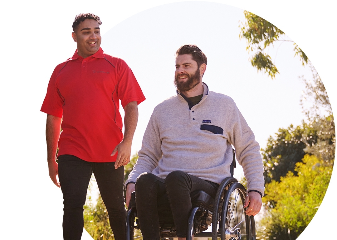 Just Better Care worker walks with participant in weelchair